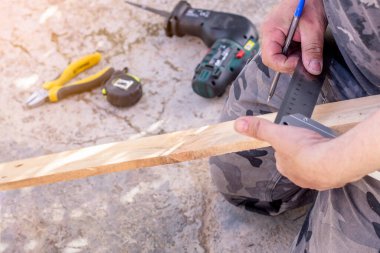 Elleri kalem ve inşaat cetvelini tutuyor ve tahta tahtaya bir çizgi çekiyor. Seçici odak
