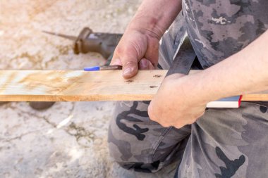 Elleri kalem ve inşaat cetvelini tutuyor ve tahta tahtaya bir çizgi çekiyor. Seçici odak
