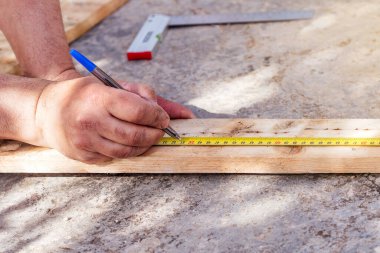 Erkek eli, tahta bir tahtayı kesmek için mezura ile ölçüyor. Seçici odak