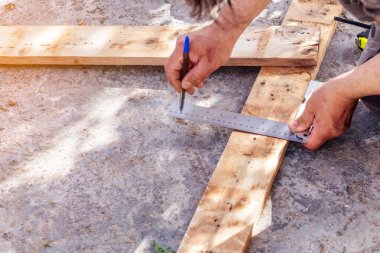 Elleri kalem ve inşaat cetvelini tutuyor ve tahta tahtaya bir çizgi çekiyor. Seçici odak