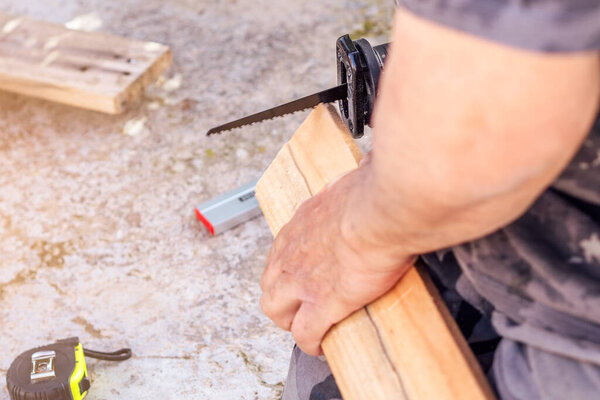 Close-up of a man cutting a plank of wood with a jig saw. Selective focus.