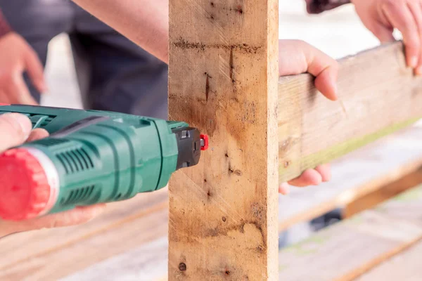 Close-up of two men nailing wooden planks with a nail gun. Selective focus.