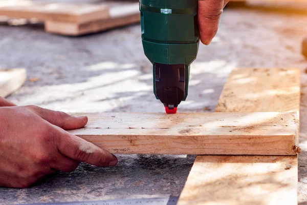 Close-up of a man\'s hands nailing wooden boards with a nail gun. Selective focus.