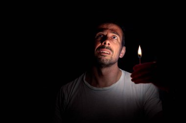 Endişeli adam karanlıkta kibritle yukarı bakıyor. Bilinç kaybı kavramı.