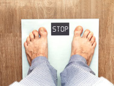 Barefoot man with scales in the bathroom, on which a stop message appears. Healthy lifestyle concept. Selective focus
