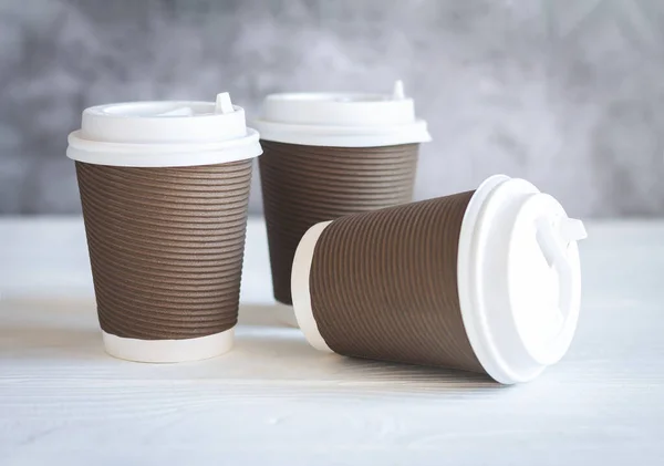 木製のテーブルの上に白い帽子を持つ3つの茶色の使い捨て紙コーヒーカップ テイクアウトドリンクと環境に優しい食器コンセプト — ストック写真