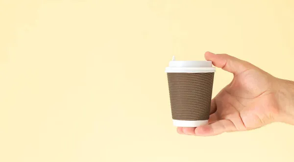 男の手は コピースペースとベージュの背景に隔離された白いプラスチックキャップと茶色の紙コーヒーカップを保持 — ストック写真