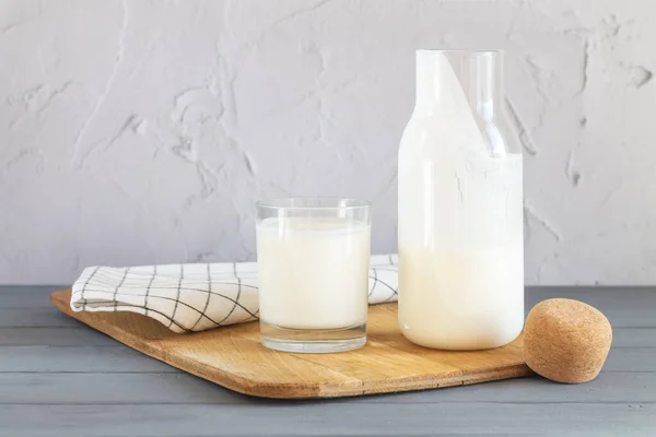自家製ヨーグルト ケフィア 発酵ミルクやサワークリームのコルクが付いているヴィンテージ瓶キッチンテーブルの上にガラスと木製のスプーンを飲むの横にある — ストック写真