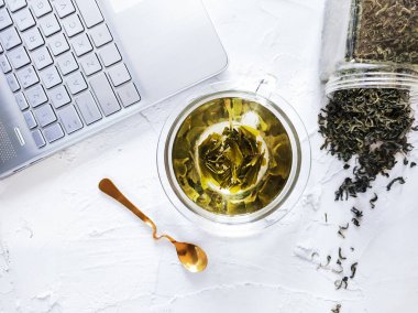 Bir bardak sıcak yeşil çay, kaşık ve dizüstü bilgisayarlı ofis masası