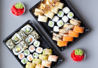 Big sushi rolls set in black plastic box for take away on gray background. Top view