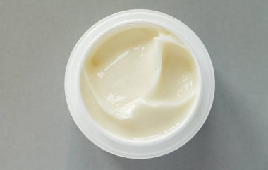 Open container of beauty treatment cream on gray background. Top view