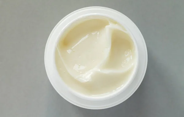 Open container of beauty treatment cream on gray background. Top view