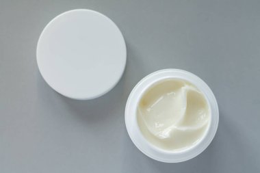 Open container of beauty treatment cream with cap on gray background. Top view