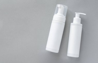 Mock-up of white plastic cosmetics bottles with skin care product on gray background. Top view