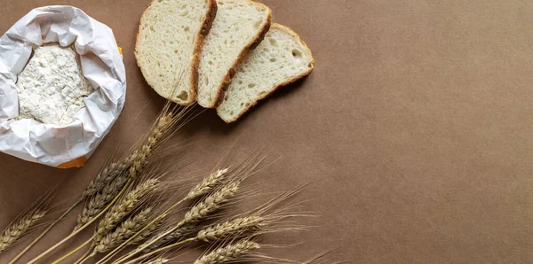 Rural kitchen or bakery background with bag of flour, slices of bread and wheat spikelets. Top view