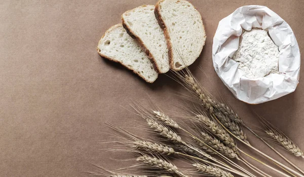 Rustic kitchen or bakery background with bag of flour, slices of fresh bread and wheat spikelets. Top view