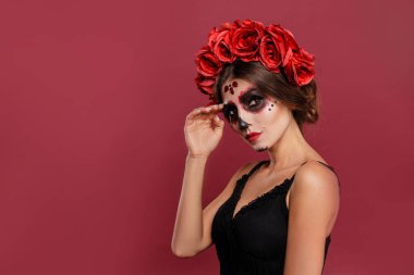 La Muerta kıyafetli ve kafataslı güzel kız pembe arka planda izole cadılar bayramı boyunca kameraya bakıyor..