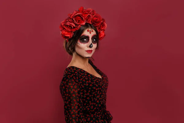 Schöne Mädchen in la muerta Kleidung und Totenkopf Make-up Blick in die Kamera während Halloween isoliert auf rosa Hintergrund. — Stockfoto