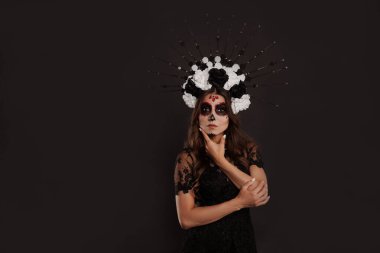 Özel siyah kıyafetli Meksikalı bir kadın beyaz kilden bir kafatası giyiyor. Profesyonel makyajla ürkütücü görünüyor.