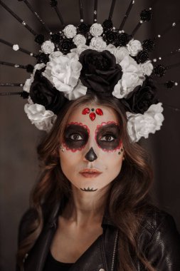 Özel siyah kıyafetli Meksikalı bir kadın beyaz kilden bir kafatası giyiyor. Profesyonel makyajla ürkütücü görünüyor.