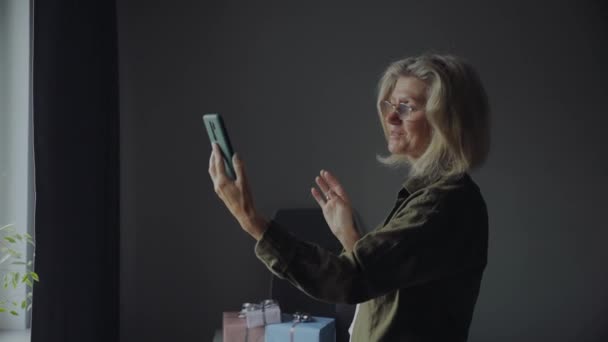 Mujer mayor feliz en gafas haciendo videollamadas con smartphone en casa — Vídeos de Stock