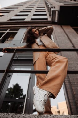  Korkulukların yanında poz veren, büyük ceketli, uzun boylu, şık bir kız ve şehrin arka planına basıyor.