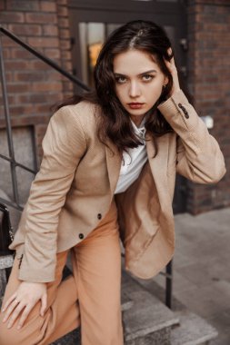  Korkulukların yanında poz veren, büyük ceketli, uzun boylu, şık bir kız ve şehrin arka planına basıyor.