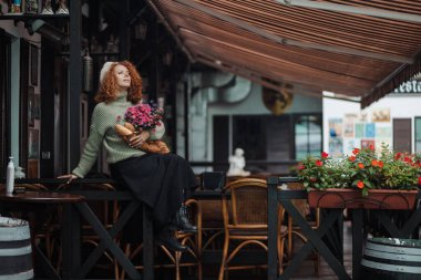 Bereli ve yeşil kazaklı bir kadın restoranın arka planında bir buket çiçek tutuyor.