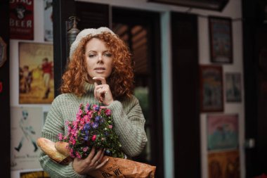 Bere kazaklı bir kadın portresi. Elinde restoranın arka planında bir buket çiçek var. 