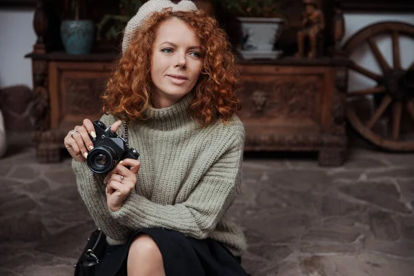 Μια γυναίκα σε ένα μπερέ και ένα πράσινο πουλόβερ κρατά μια κάμερα στα χέρια της και παίρνει πλάνα — Φωτογραφία Αρχείου