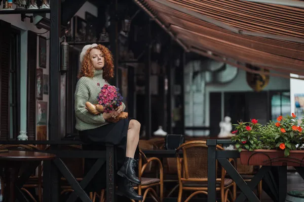 Una mujer en una boina y un suéter verde sostiene un ramo de flores sobre un fondo de restaurante — Foto de Stock