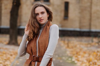 Sonbahar parkında gri elbiseli gülümseyen genç kızın portresi. 