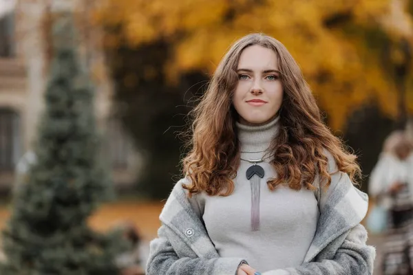 Retrato de una joven sonriente con un abrigo gris en el parque de otoño —  Fotos de Stock