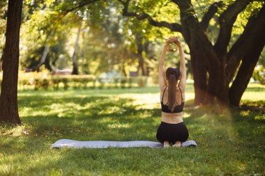  Spor üniformalı genç bir kadın şehir parkında rahatlayıp meditasyon yapıyor..