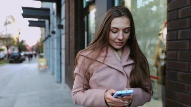 Ceketli, yürüyen ve cep telefonu kullanan güzel, uzun saçlı bir kadın.