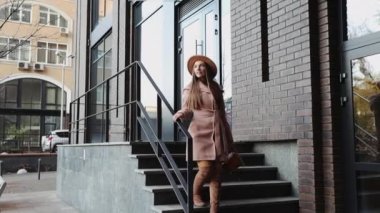 Paltolu ve şapkalı bir kadın ofis arka planındaki merdivenlerden aşağı iniyor.