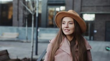 Paltolu ve yuvarlak şapkalı güzel bir kadın modern şehir arka planında yürüyor.