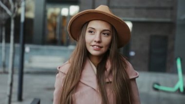 Paltolu ve yuvarlak şapkalı güzel bir kadın modern şehir arka planında yürüyor.