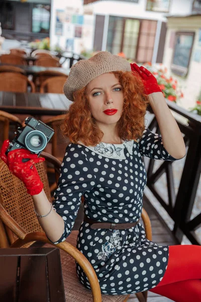 Una mujer en una boina y vestido vintage sostiene una cámara en sus manos y toma disparos — Foto de Stock