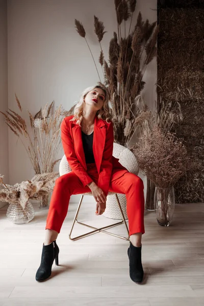 Молодая стильная блондинка в красном костюме сидит на стуле — стоковое фото