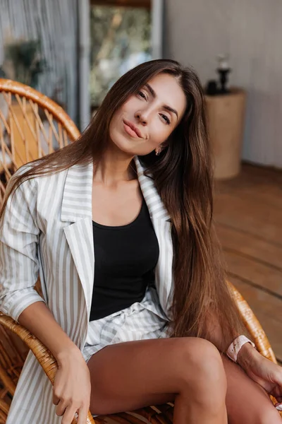 Bella donna bruna con i capelli lunghi in una giacca bianca a riposo in un bungalow — Foto Stock