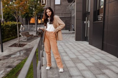Büyük montlu, uzun boylu, modern bir kız ofis binasının girişinde duruyor.
