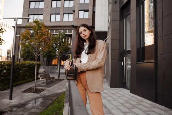 Alta chica moderna en una chaqueta de gran tamaño se encuentra cerca de la entrada a la construcción de la oficina — Foto de Stock