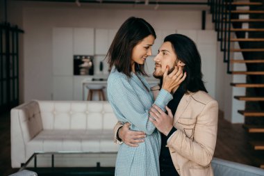 Genç koca, karısına oturma odasında nazikçe sarılıyor.