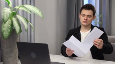 Evde üzgün bir adam üniversiteden ya da üniversiteden gelen mektupları okuyor.