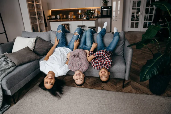 Feliz familia mamá y dos hijos tonteando y tumbados boca abajo en el sofá —  Fotos de Stock