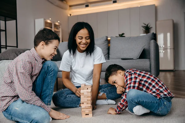 Een gelukkige zwarte familie moeder en twee zonen die een rondje jenga verwennen. — Stockfoto