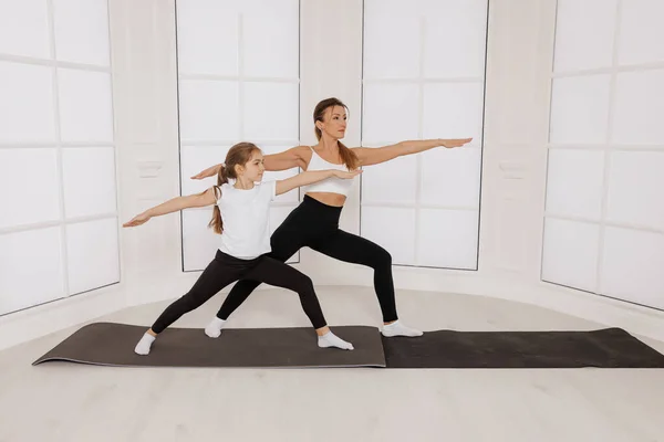 Ioga prática mulher yogi e menina criança treino no estúdio de pé em pose de guerra — Fotografia de Stock