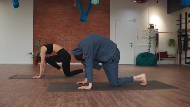 Чоловік і жінка роблять синхронну вправу на розтяжці ніг на підлозі мат в студії йоги — стокове відео
