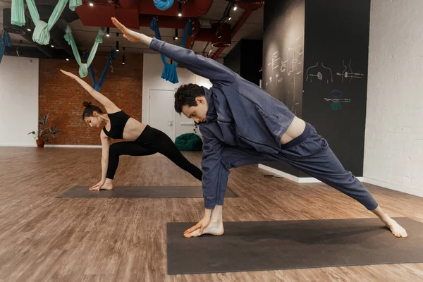 Grupo de jovens praticando ioga com treinador em estúdio espaçoso de ioga — Fotografia de Stock